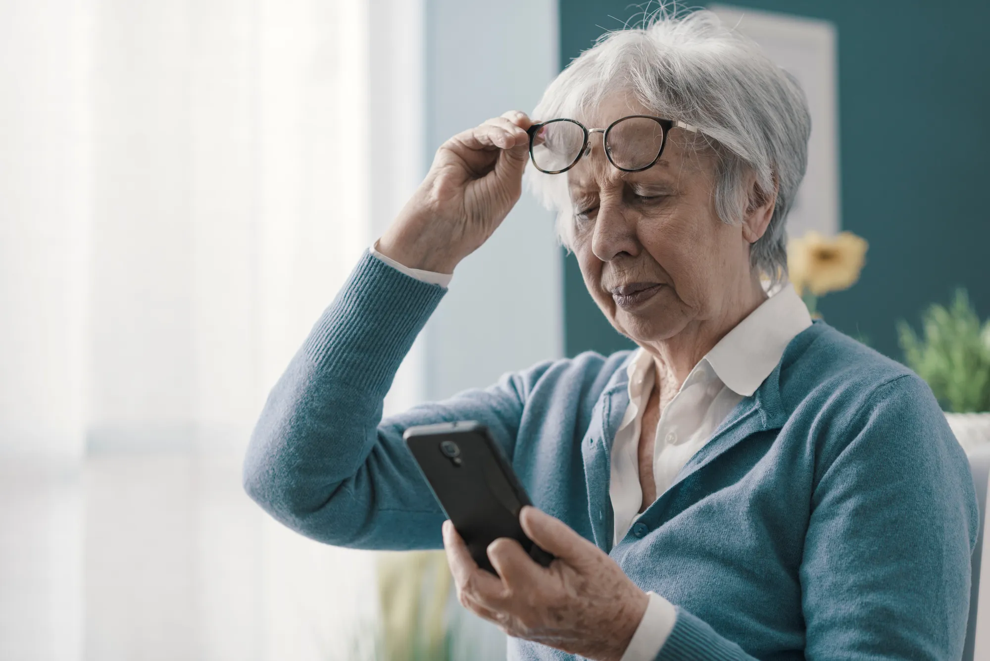 Ältere Frau liest auf dem Smartphone und hebt ihre Brille an