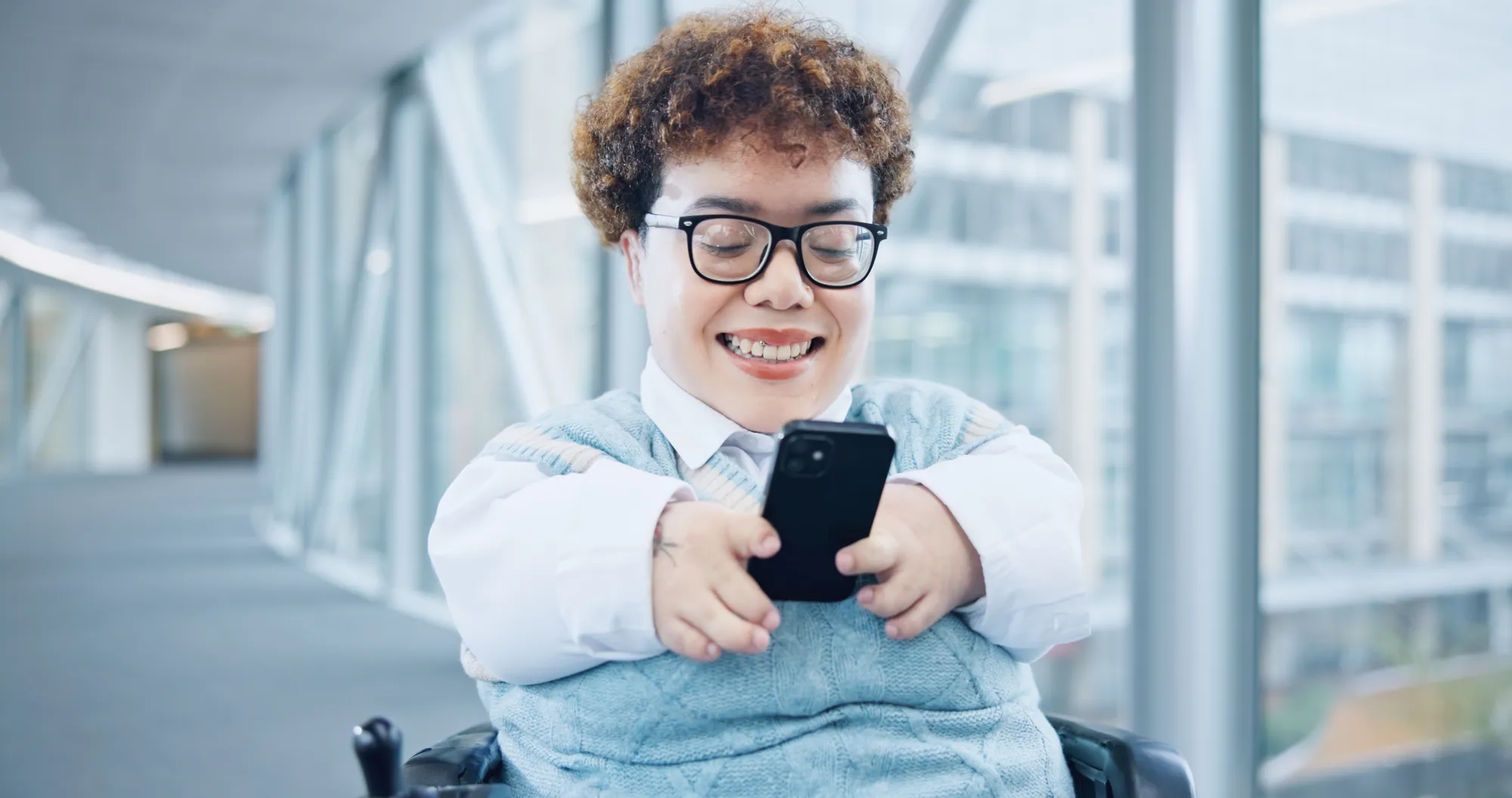 Lächelnde junge Person im Rollstuhl benutzt ein Smartphone